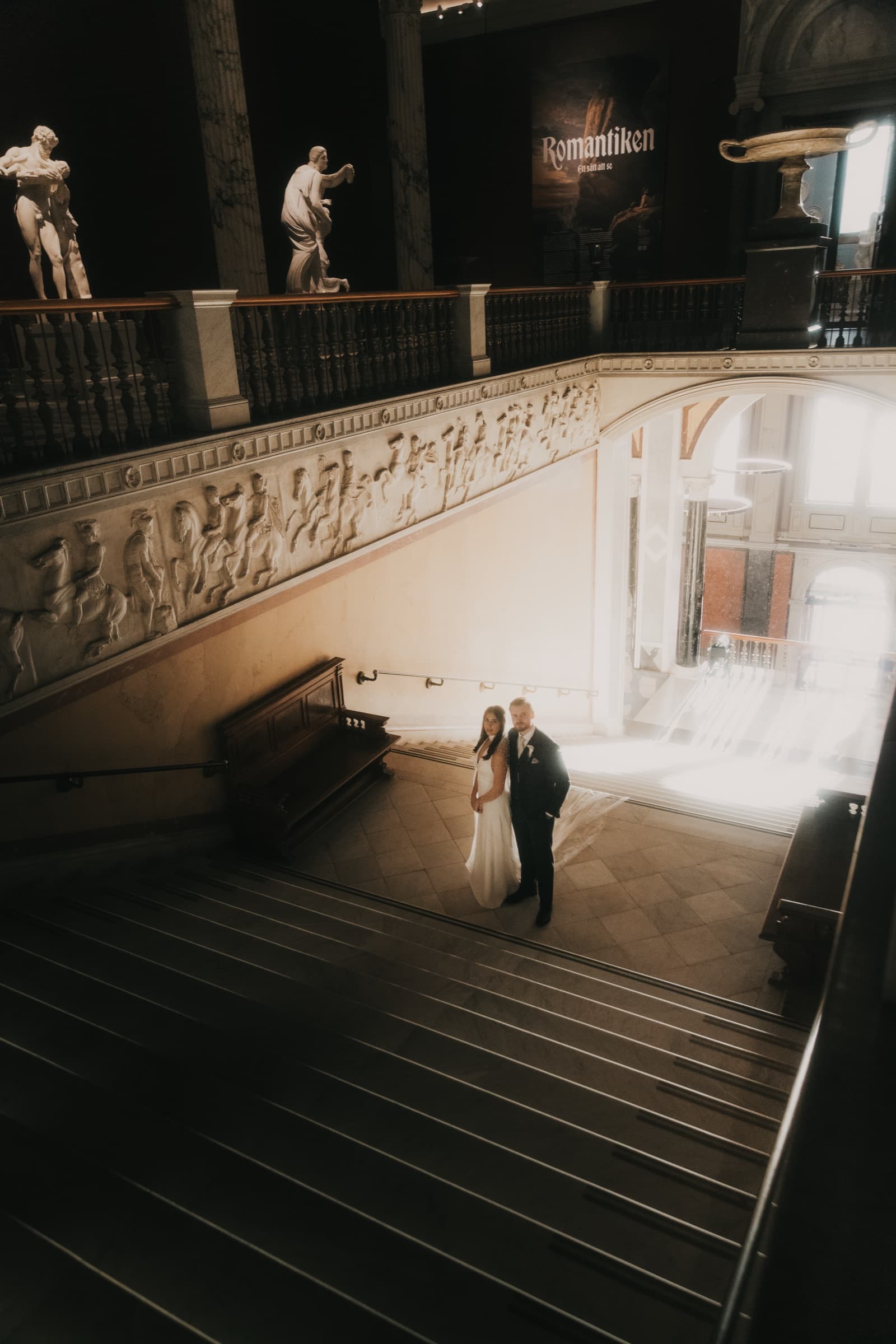 Couple small in frame on Nationalmuseum's grand staircase among sculptures