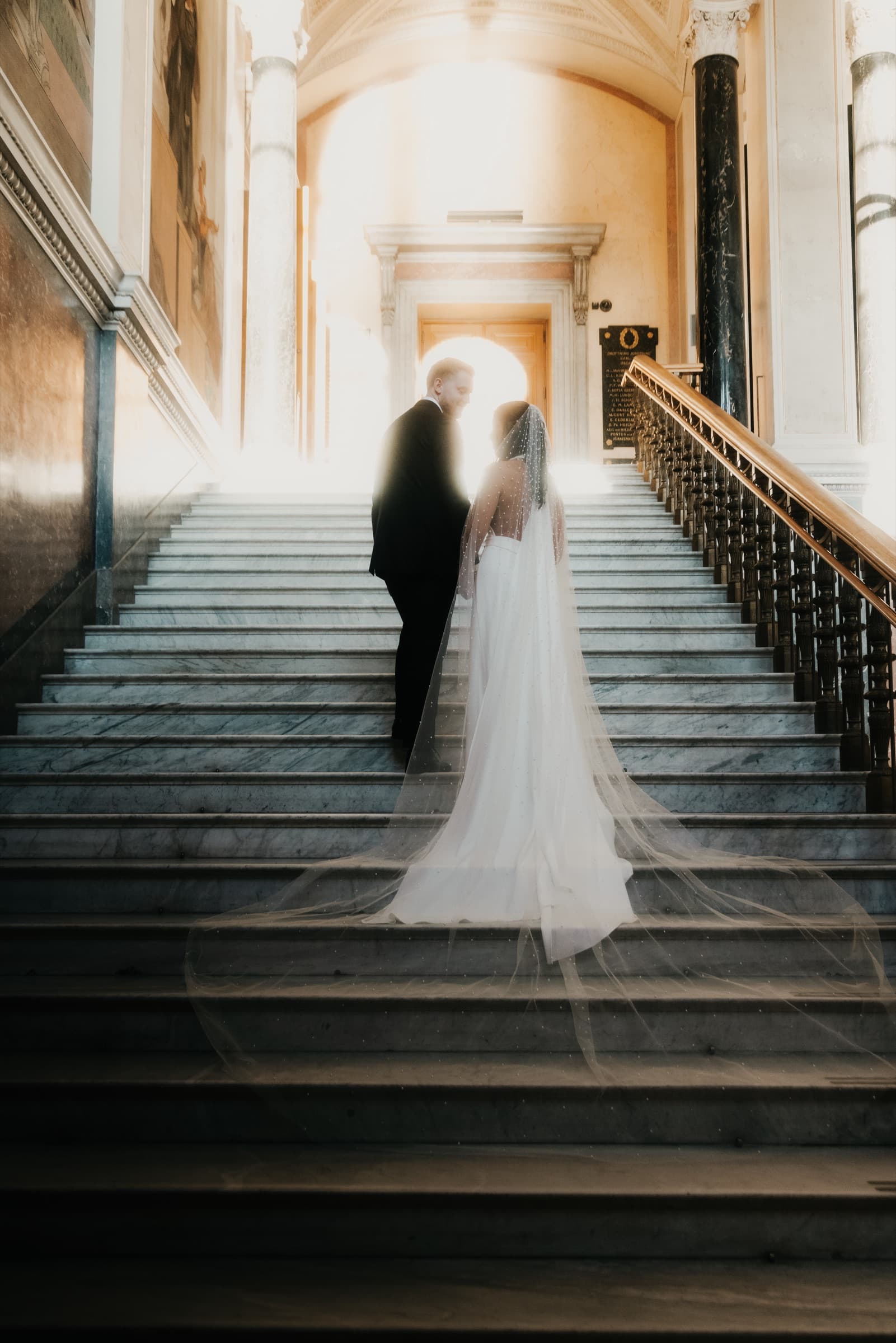 Couple backlit on the grand staircase, veil flowing in a long train