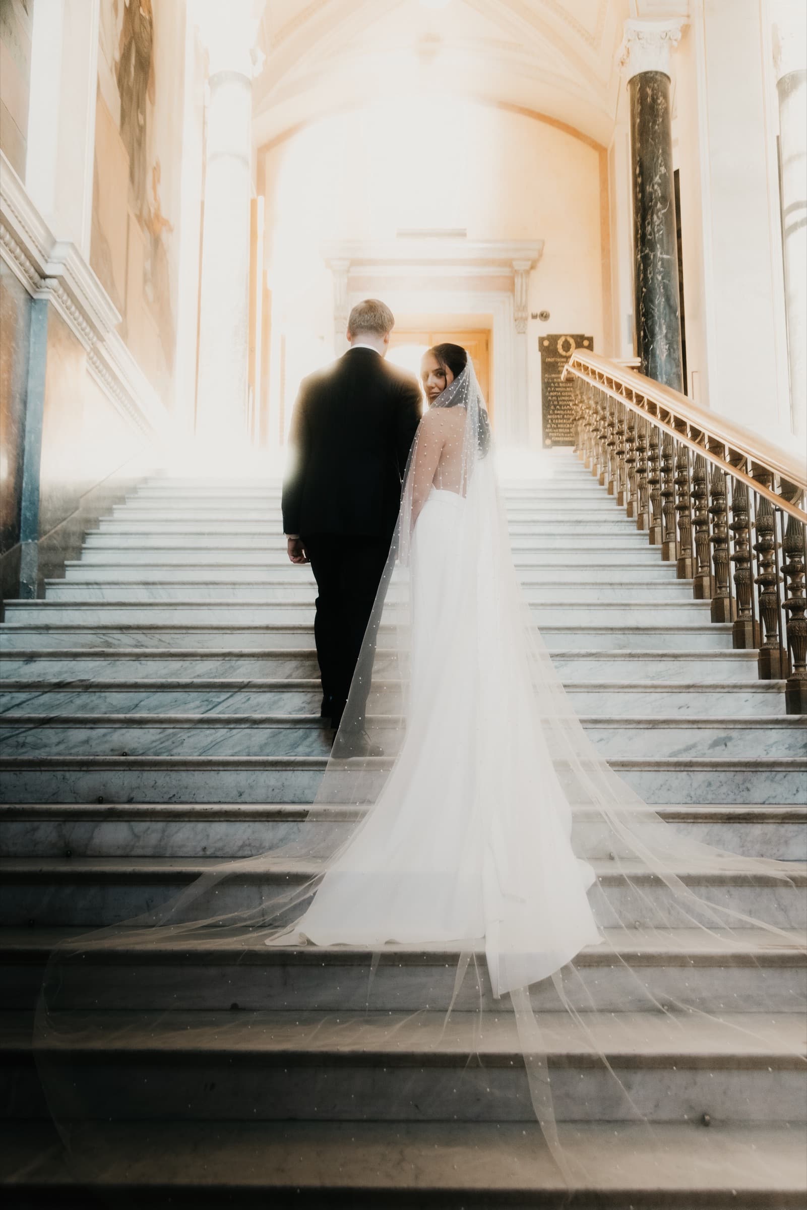 Couple ascending the marble staircase, the bride's long train trailing behind
